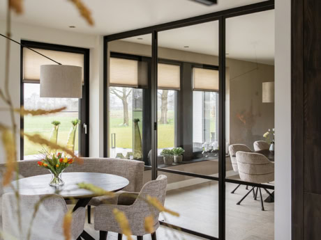 Moderne vouwdeuren van staal in een lichte woonkamer met uitzicht op tuin.