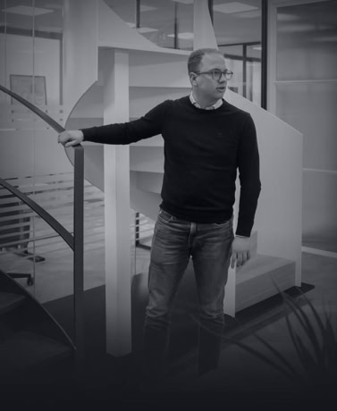 Man in zwart shirt en jeans in modern kantoor met glazen balustrade.