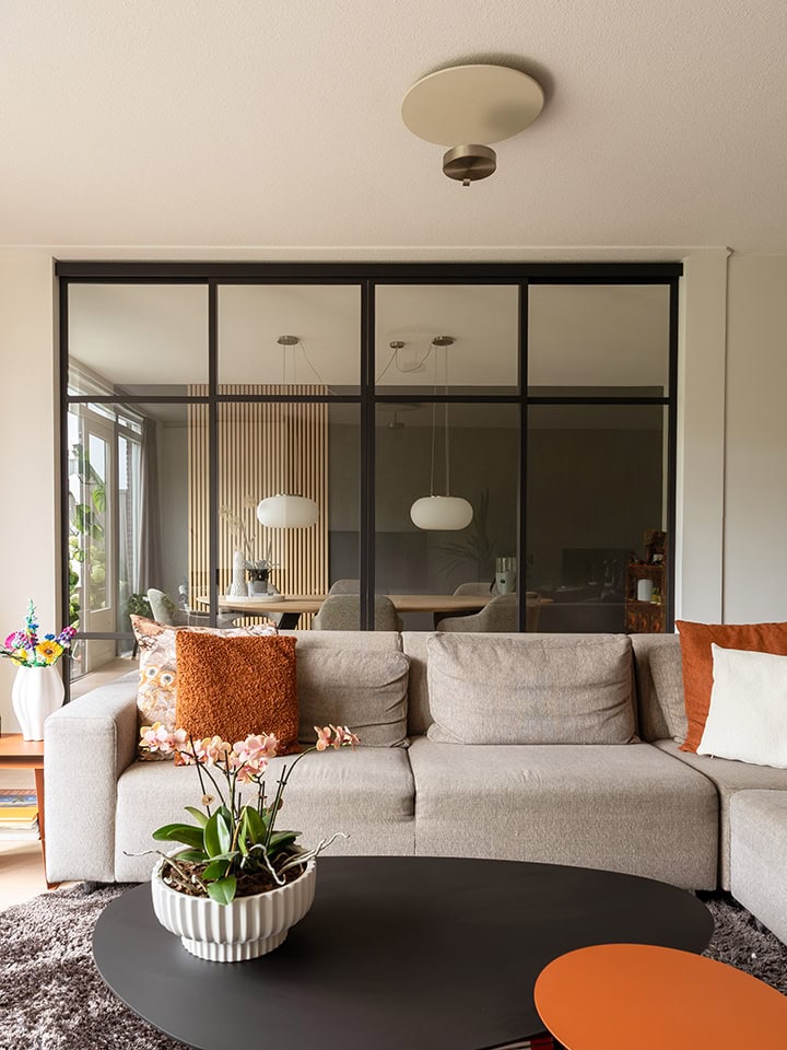 Moderne schuifdeur van staal en glas in woonkamer met natuurlijke lichtinval.