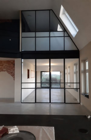 Moderne stalen schuifdeur met grote glazen panelen in een industrieel interieur.