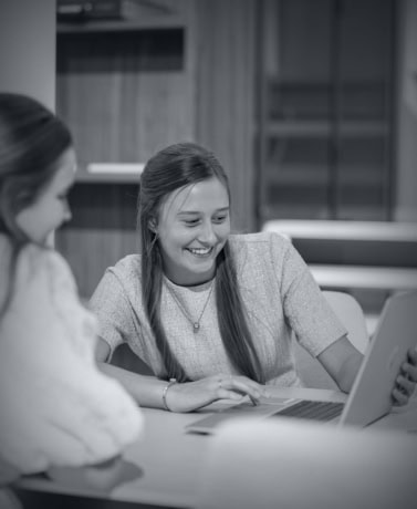 Vrouw met lang haar kijkt lachend naar laptop scherm tijdens gesprek.