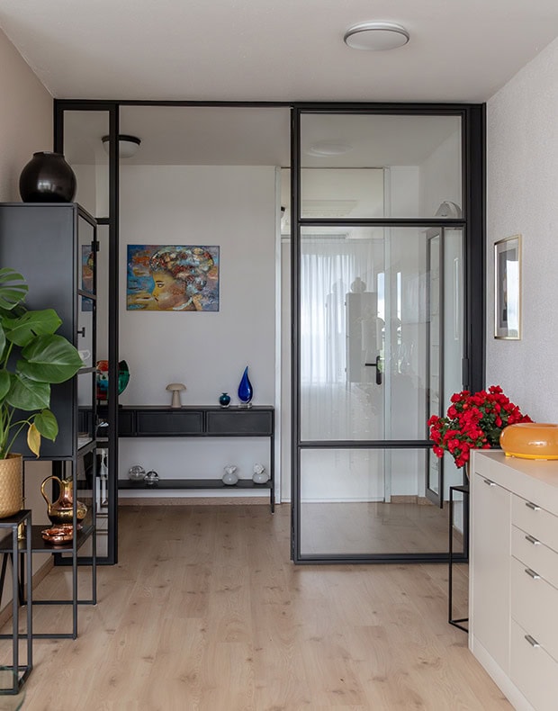 Moderne vouwdeuren van zwart staal en glas in interieur met planten en decoratie.