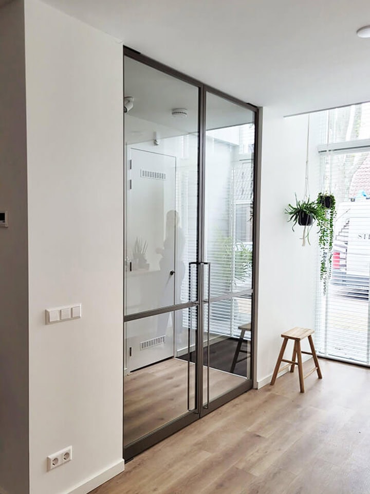 Moderne glazen scheidingswand in een lichte woonkamer met houten vloer.