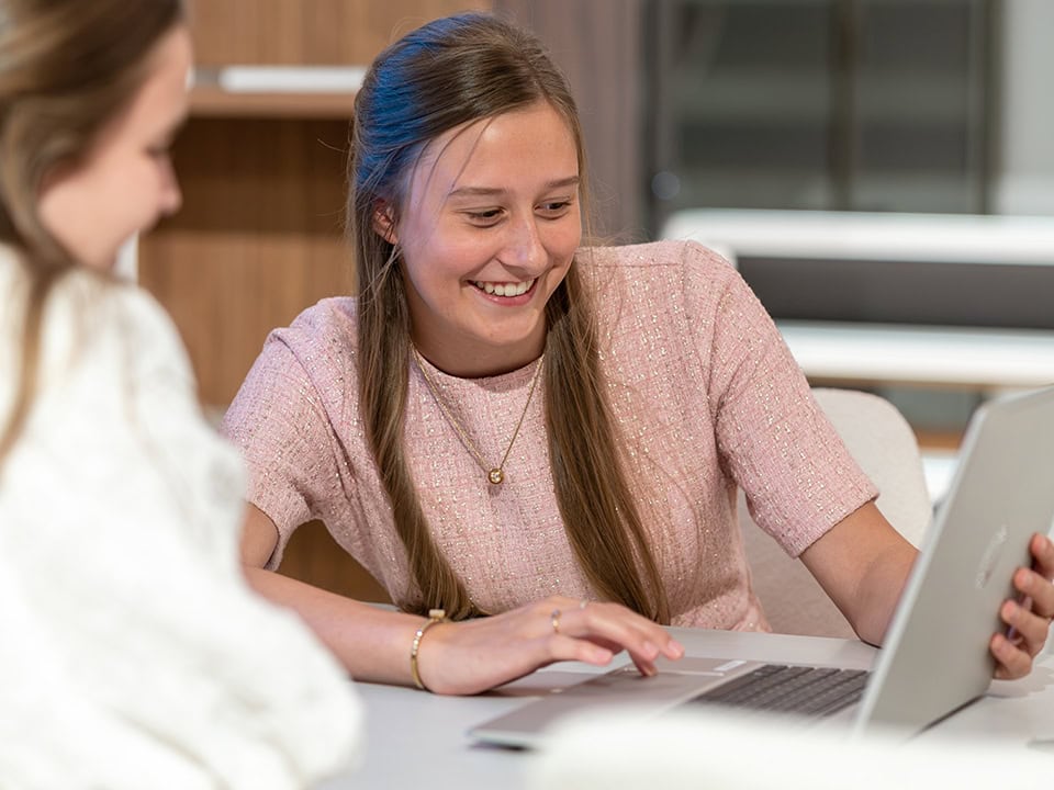 Vrouw kijkt blij naar laptop tijdens werk of studie in kantooromgeving.